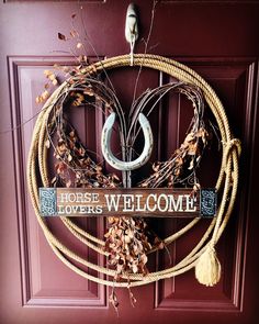 a wreath is hanging on the door with a horse shoe and welcome sign attached to it