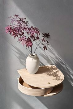 a white vase sitting on top of two wooden trays next to a purple plant