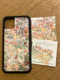 the phone case is next to an envelope and card holder on the floor with flowers