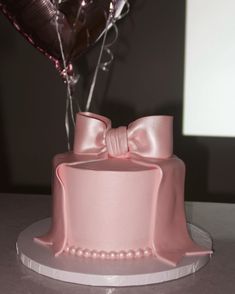 a pink cake decorated with pearls and a bow