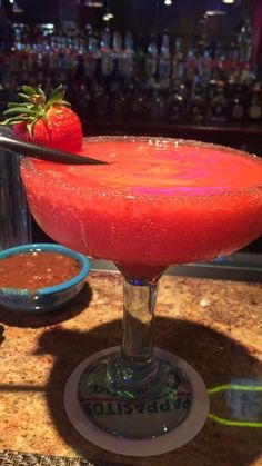 a red drink sitting on top of a counter next to a bowl of strawberries