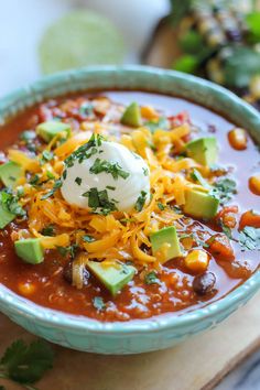 a bowl of chili soup with sour cream and avocado garnish on top