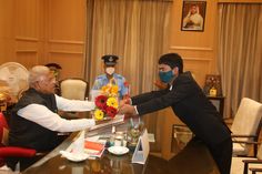 two men in suits and face masks are shaking hands with each other at a table