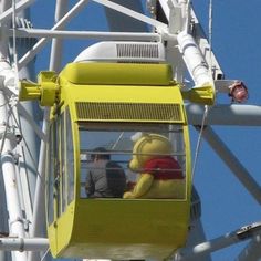 a yellow ferris wheel with two people on it and one person in the top seat