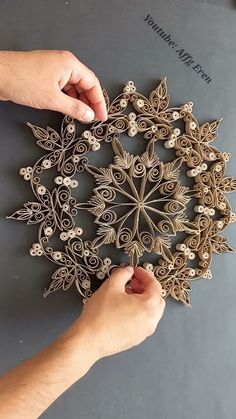 two hands are working on an intricately designed paper doily that is being held by another hand