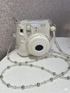 a white camera sitting on top of a table next to a silver beaded chain