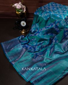 a blue silk sari with white flowers on it and a gold vase next to it