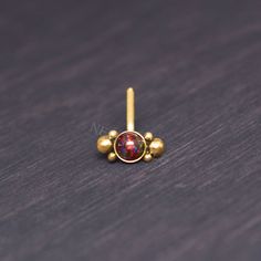 a gold nose ring with a red stone in the center on a wooden surface,