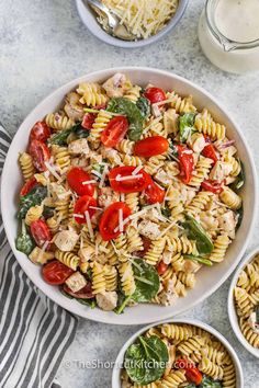 pasta salad with chicken, tomatoes and spinach in a white bowl on a marble table