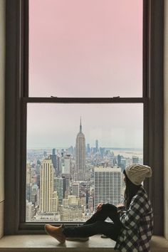 a person sitting on a window sill looking out at the empire building in new york city