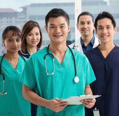 four doctors are standing together in front of a hospital building and one is holding a clipboard