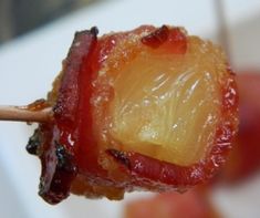 a close up of food on a toothpick with fruit in the back ground