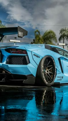 a blue sports car parked in front of a palm tree on a wet parking lot