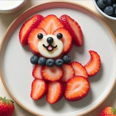 a white plate topped with strawberries and a dog shaped cookie on top of it