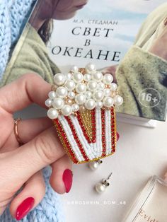 a close up of a person's hand holding a brooch with pearls on it