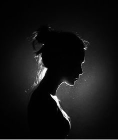 a black and white photo of a woman's profile in the dark with her hair pulled back