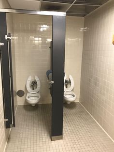 two urinals in a public restroom with tiled floors and walls, one is black and the other is white