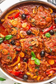 a pan filled with meat and vegetables covered in marinara sauce, garnished with fresh basil leaves