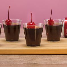 four glasses with chocolate pudding and cherries in them on a wooden tray next to a can of jelly