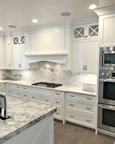 a large kitchen with white cabinets and marble counter tops, along with stainless steel appliances