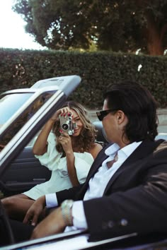 a man and woman sitting in a car taking pictures