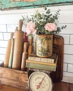 a clock and some books on a table with flowers in a vase next to it