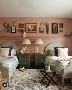 two beds in a bedroom with pink walls and pictures on the wall above them,