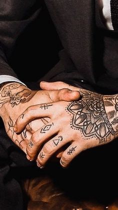 a man in a suit and tie with tattoos on his arm holding another mans hand