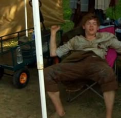 a man sitting in a chair with his arms up and mouth wide open next to a tent