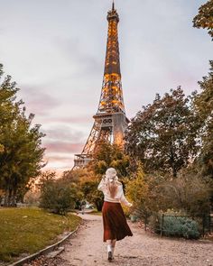 a woman walking down a path in front of the eiffel tower