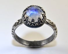 This moonstone ring features a faceted 8mm rainbow moonstone, a romantic piece with a white gemstone that has a nice blue flash. The sterling silver ring features a stone that is set in a beautifully detailed and decorative crown gallery wire. This statement ring is shown oxidized for an antique look, but I can also make it highly polished for a more classic look or for a wedding ring. Please select your preferred finish during the ordering process. The beautiful Renaissance style band with scro Mystical Sterling Silver Moonstone Wedding Ring, Silver Faceted Moonstone Ring For Wedding, Silver Faceted Moonstone Wedding Ring, Faceted Silver Moonstone Wedding Ring, June Birthstone Jewelry, June Birthstone, Jewelry Wedding, Moonstone Ring, June Birth Stone