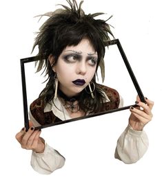 a woman with black makeup holding up a mirror