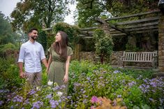 a man and woman standing next to each other in the middle of a garden filled with purple flowers