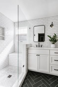 a white tiled bathroom with black and white tile flooring, large mirror on the wall