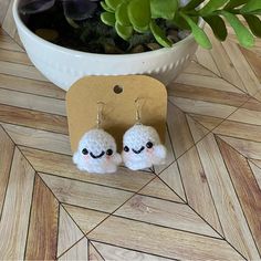 small white crocheted sheep earrings sitting next to a potted plant