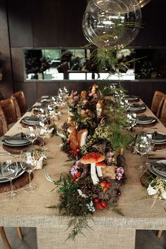 a long table is set with plates and place settings for an outdoor dinner party in the woods