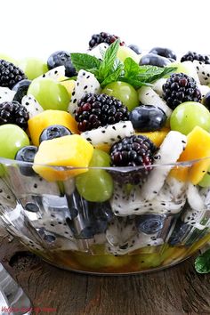 a glass bowl filled with fruit salad on top of a wooden table