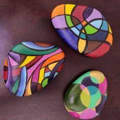 three colorful rocks sitting on top of a wooden table next to each other with circles painted on them