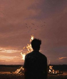 a man standing in front of a fire with birds flying over it at sunset or dawn