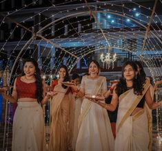 three women in sari are holding trays with lights on them and one woman is smiling at the camera