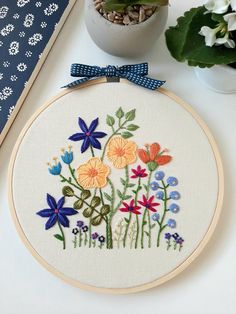 an embroidery kit with flowers on it next to a potted plant