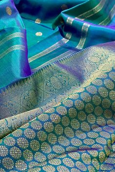 The stunning kanjivaram saree in cobalt blue shot with bottle green is handwoven with rudraksham motifs woven in gold zari, allover the body. The borders have chevron and geometric patterns in gold zari with a green selvedge.The grand pallu features rudraksham motifs flanked by peacock, yazhi along with traditional motifs in gold zari. Approximate Length 6.5 mtrs (inclusive of blouse length) Height - 46 - 52" Approximate weight - 1.6 lbs Saree comes with fall, picot and tassels done. Blouse piec Blue Shots, Kanjivaram Sarees, Silk Cotton Sarees, Blouse Length, Blouse Piece, Cotton Saree, Cobalt Blue, Silk Sarees, Geometric Pattern