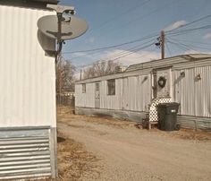 an old train car sitting on the side of a dirt road next to a building