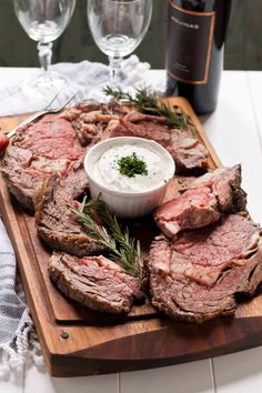 a wooden cutting board topped with sliced up meat next to two wine glasses and a bottle