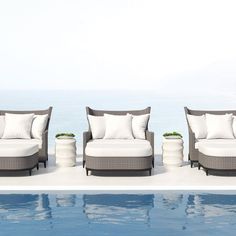 three lounge chairs sitting next to a swimming pool with pillows on the back and sides