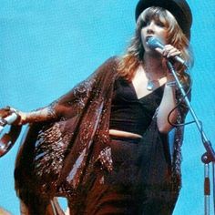 a woman standing on top of a stage holding a microphone in her hand and wearing a black hat