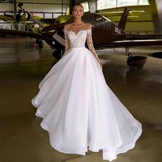 a woman standing in front of an airplane wearing a wedding dress with long sleeves and beading