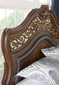 an ornate wooden bed frame with white and blue pillows on it's headboard