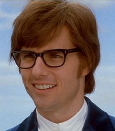 a man wearing glasses and a suit smiling at the camera with sky in the background