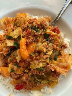 a white plate topped with meat and vegetables on top of rice next to a fork